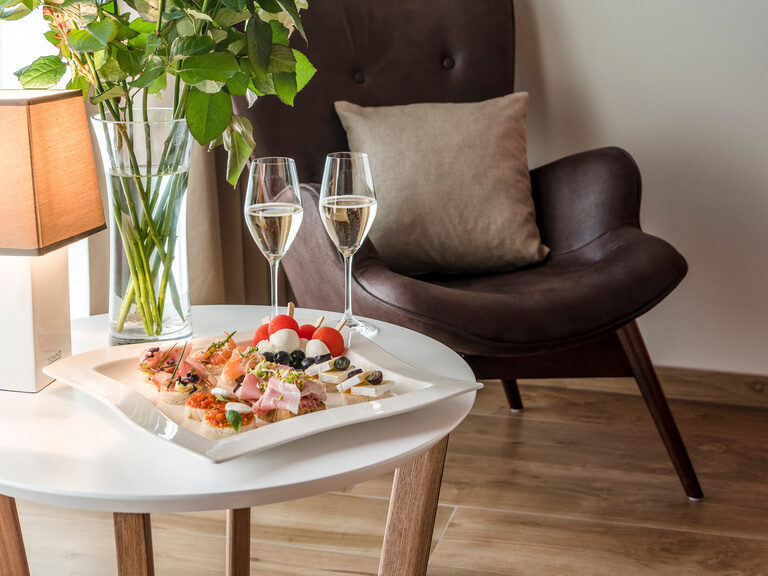 Ein einladender Tisch mit einem Speisetablett und Blumenarrangement als Begrüßungsgeschenk in der Private Spa Suite des Wellnesshotels Mooshof im Bayerischen Wald..