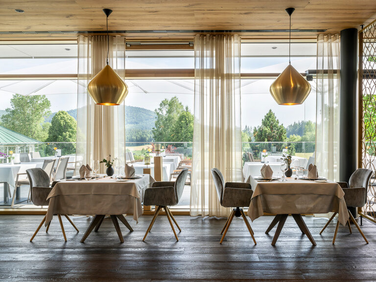 Gemütliches Ambiente und Blick auf den Bayerischen Wald im Restaurant vom Wellnesshotel Mooshof mit feinem Besteck und edlen Tischdecken.