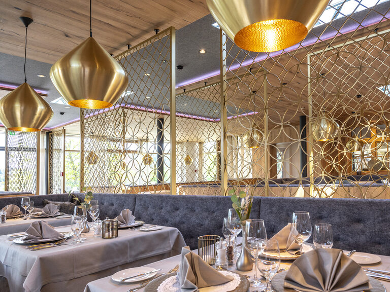 Feines Dinnerambiente mit edel eingedeckten Tischen und luxuriöser goldener Dekorationen im Restaurant des Wellnesshotels Mooshof in Bayern.