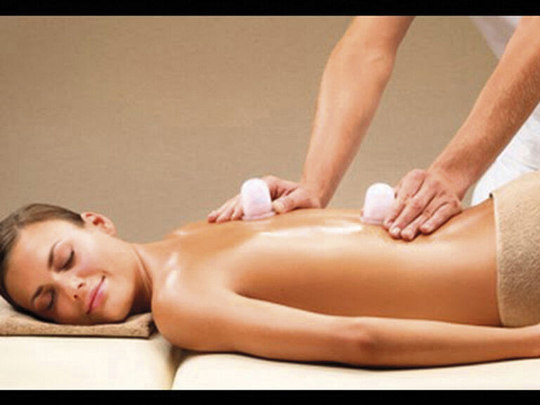 Auf einem Massagetisch des Hotels Mooshof in Bayern liegt eine Frau und erhält eine entspannende Rückenmassage mit Eiswürfeln.