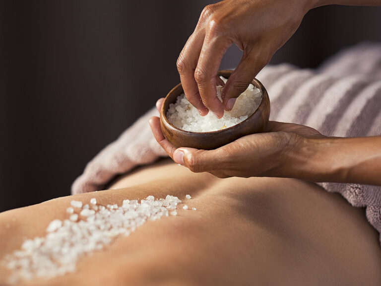 Eine Frau erhält eine Salzbehandlung auf dem Rücken im erstklassigen Wellnessbereich des Hotels Mooshof..