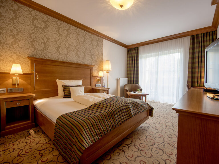 Gemütliche Wohnatmosphäre mit einem großzügigen Bett und Flachbildfernseher in der Single-Suite mit Nordbalkon im Wellnesshotel Mooshof im Bayerischen Wald.