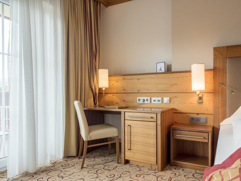 Der stilvolle Raum in der Gartensuite Schwalbennest des Wellnesshotels Mooshof in Bayern mit praktischem Schreibtisch und Stuhl neben dem komfortablen Doppelbett.