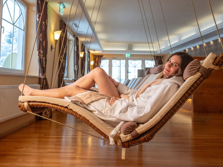 Eine Frau entspannt sich auf einer Schwebeliege im lichtdurchfluteten Ruhebereich des Wellnesshotels Mooshof im Bayerischen Wald.