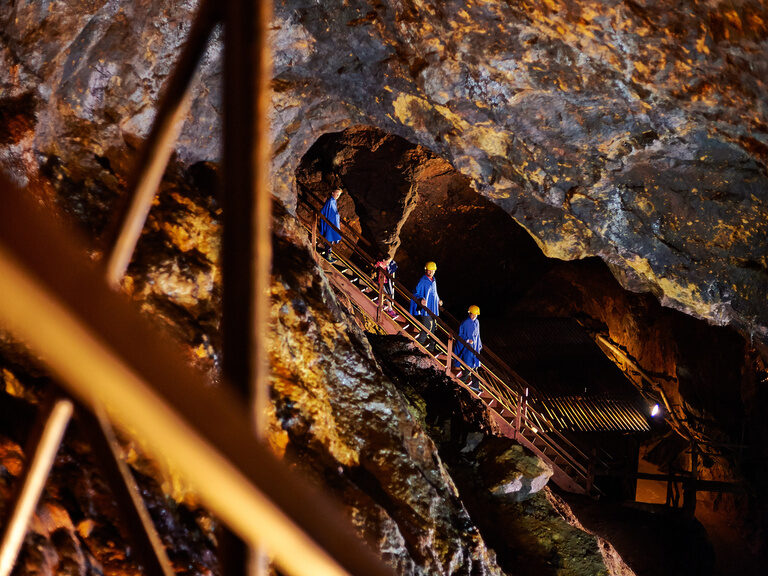 Besucher steigen auf einer Holztreppe durch das beleuchtete Silberbergwerk Bodenmais im Bayerischen Wald.