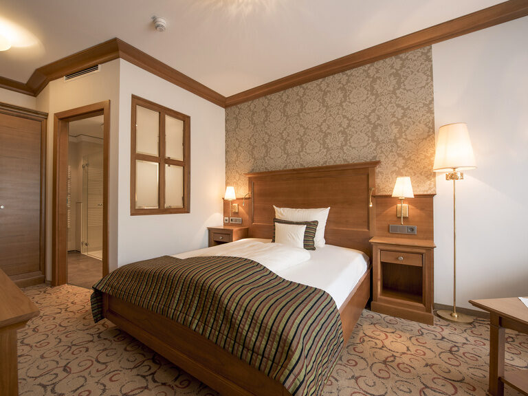 Einladender Schlafbereich der Single-Suite des Wellnesshotels Mooshof in Bodenmais mit bequemen Bett und harmonischer Beleuchtung.