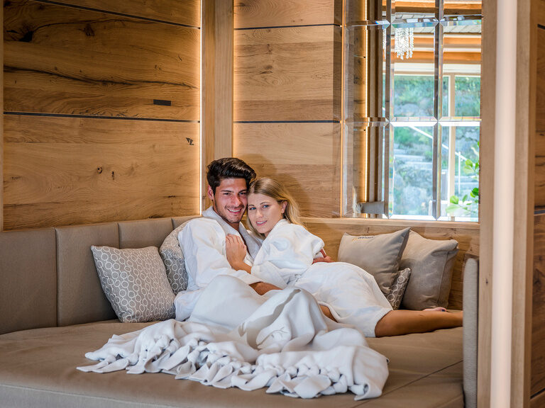 Gemütliche Sitzecke im Wellnessbereich vom Wellnesshotel Mooshof in Bayern mit einem Paar in entspannter Pose im Fokus.