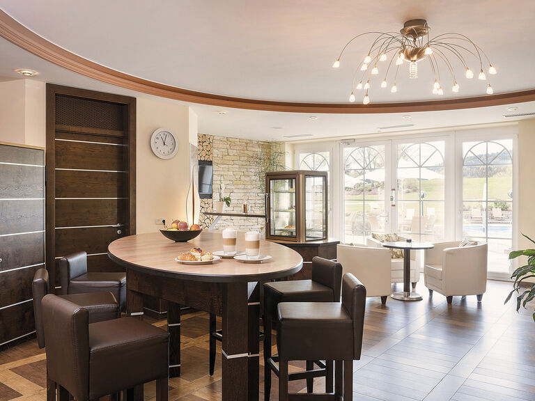 Einladende Essplatzgestaltung im Spa Bistro des Wellnesshotels Mooshof in Bodenmais mit Obstschale und Kaffe auf einem Tisch in einem entspannenden Ambiente.