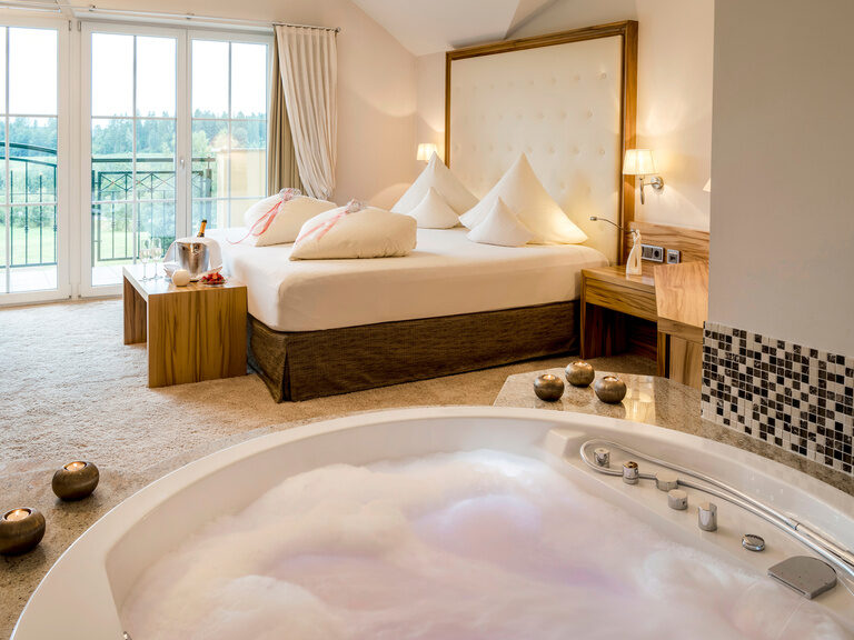 Das luxuriöse Doppelbett und eine schäumende Badewanne in der Honeymoonsuite des Wellnesshotels Mooshof im Bayerischen Wald.