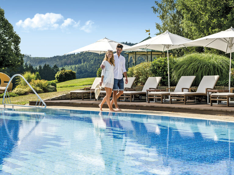 Ein Paar spaziert entlang des Außenpools im Wellness & SPA Resort Mooshof.