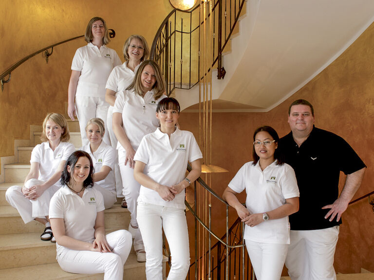 Das Team des Vitalresorts in lockerer Gruppierung auf Stufen im Wellnesshotel Mooshof im Bayerischen Wald.