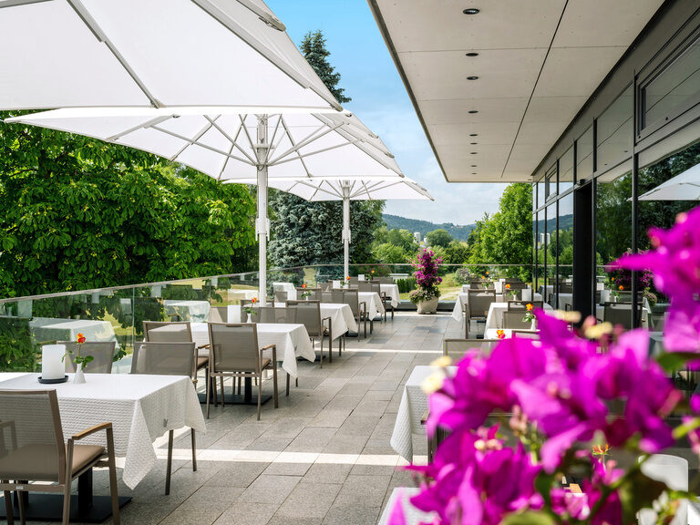 Möblierter Essbereich des Hotels Mooshof mit Sonnenschutz auf der Außenterrasse mit Panoramablick auf den Bayerischen Wald.