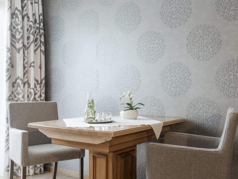 Ein gemütlicher Tisch mit floraler Dekoration und Stühlen, der im Wohnbereich der Lohwiessuite im Wellnesshotel Mooshof in Bodenmais steht.