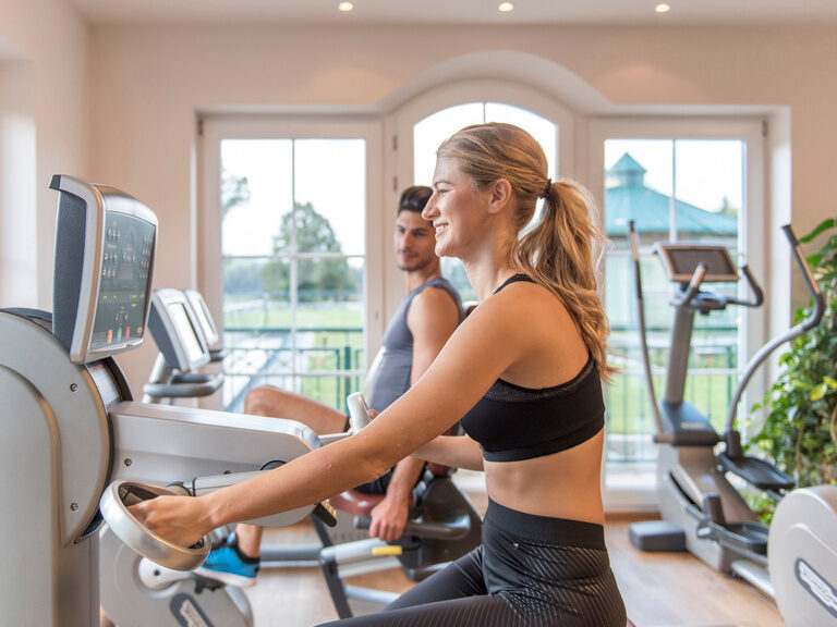 Eine Frau trainiert auf einem Fahrrad im Fitnessraum des Wellnesshotels Mooshof im Bayerischen Wald.