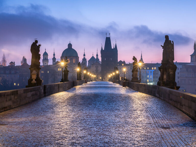 Die Karlsbrücke bei Sonnenuntergang in Prag spiegelt sich im Fluss wider.