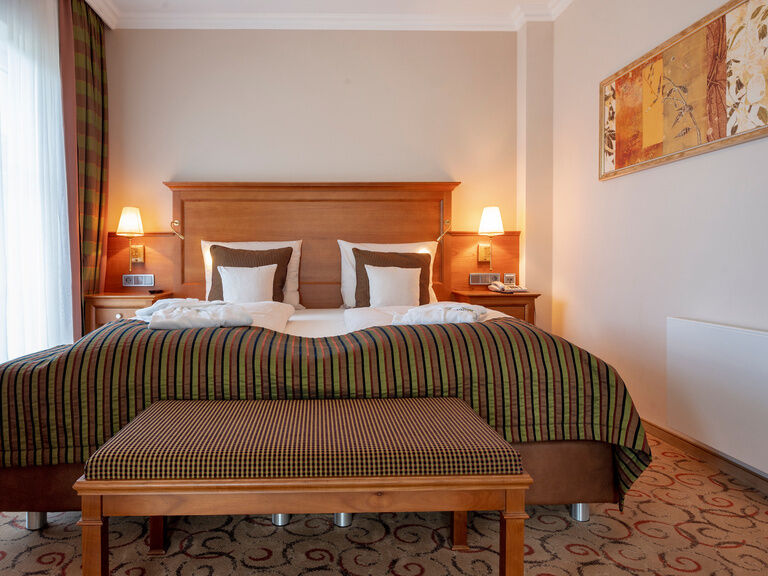 Das gemütliche Doppelbett in der Turmsuite Hochzell des Wellnesshotels Mooshof, flankiert von zwei Nachttischlampen, die eine harmonische Beleuchtung schaffen.