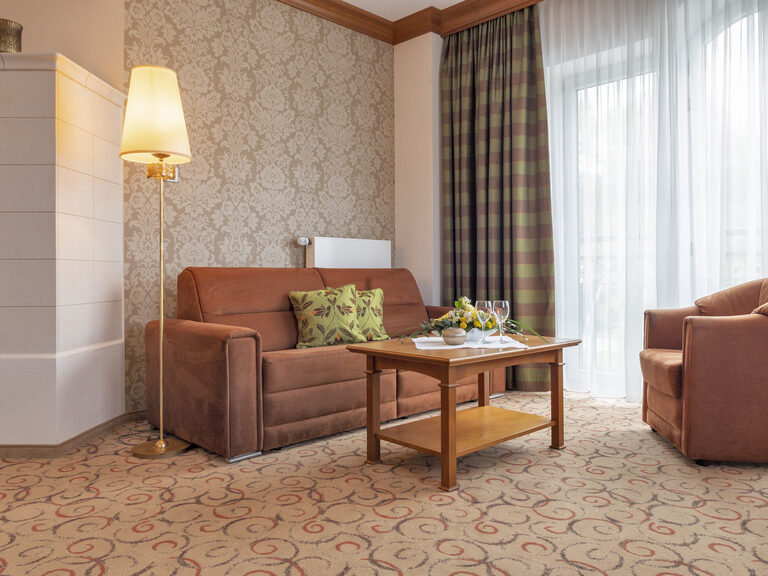 Das einladende Wohnzimmer mit einem Sessel und einer Couch in der Turmsuite Hochzell des Wellnesshotels Mooshof im Bayerischen Wald.