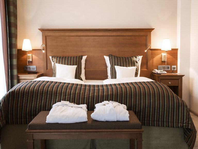 Die Turmsuite Hochzell im Wellnesshotel Mooshof im Bayerischen Wald zeigt ein geschmackvoll eingerichtetes Schlafzimmer mit einem luxuriösen Bett und zwei eleganten Lampen.