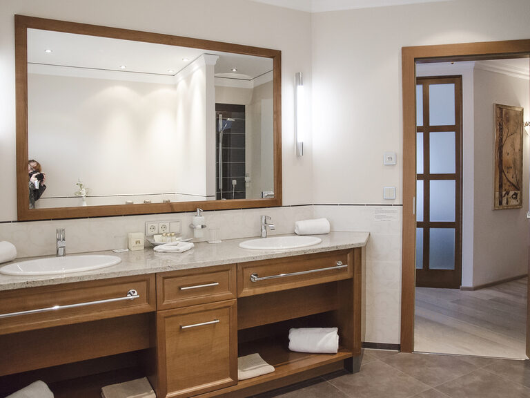 Modernes Badezimmer mit zwei Waschbecken und einem großen Spiegel in der Turmsuite Kronberg des Wellnesshotels Mooshof in Bodenmais.
