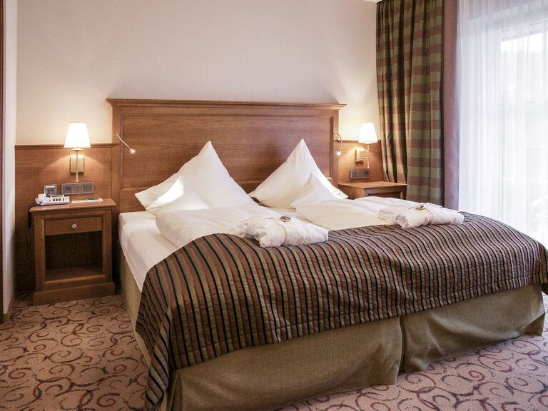 Elegantes Schlafzimmer in der Turmsuite Kronberg des Wellnesshotels Mooshof im Bayerischen Wald mit einem komfortablen Bett mit feinsten Stoffen und stilvollen Lampen.