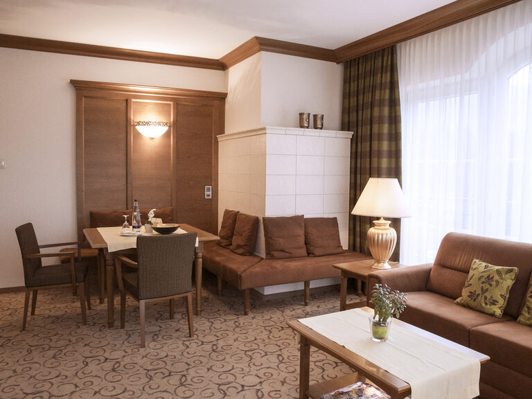 Charmantes Wohnzimmer mit Kachelofen und hochwertigen Möbeln in edlem Kirschholz in der Turmsuite Kronberg des Wellnesshotels Mooshof in Bayern.