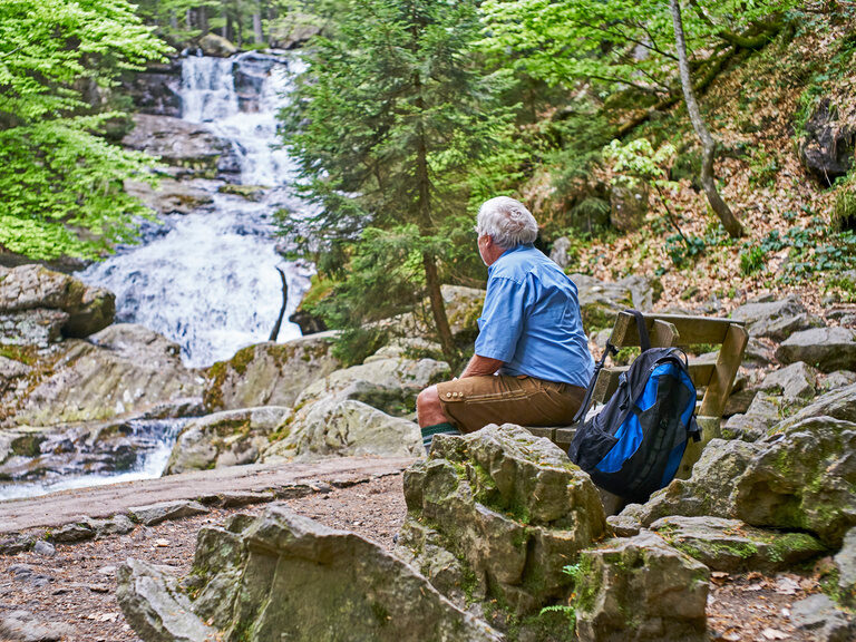 Eine Person rastet vor einem Wasserfall und genießt einen schönen Tag beim Wandern.