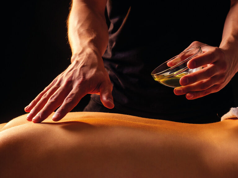 Ein Moment der Entspannung im stilvollen Wellnessbereich des Wellnesshotels Mooshof in Bayern bei einer Rückenmassage mit wohltuenden Öl.