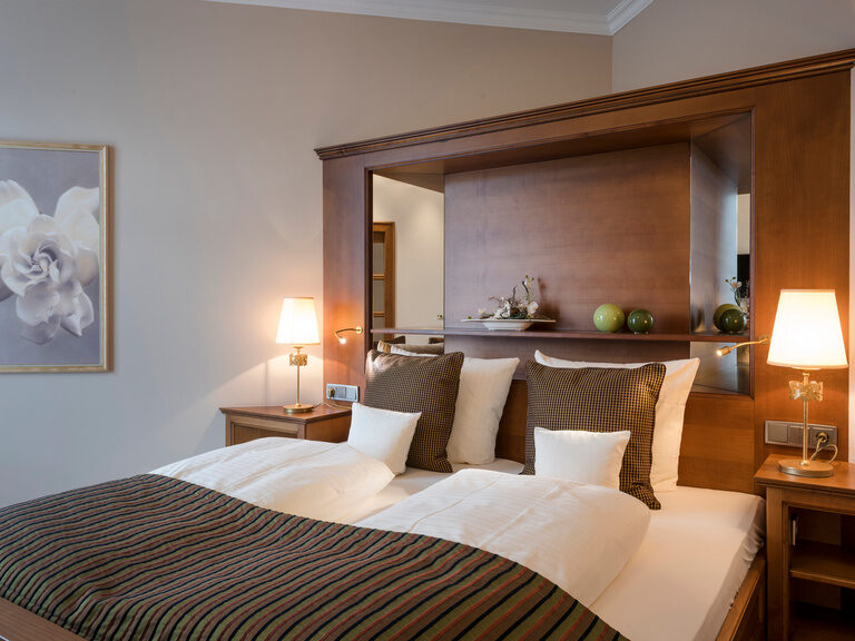 Bequemes Bett in der Wellnesssuite Bergzauber des Wellnesshotels Mooshof in Bayern mit akzentuierten Wurfkissen und einem modernen Bettrahmen aus Kirschholz.