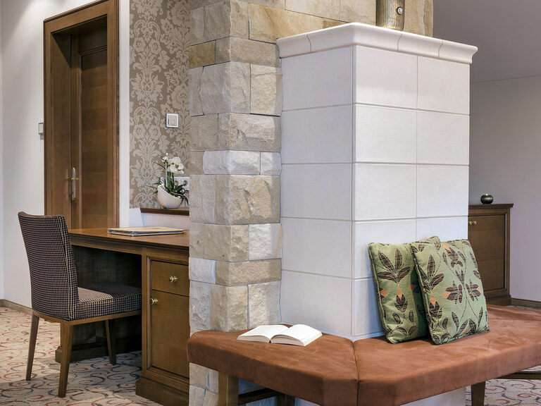 Gemütliches Wohnzimmer mit Sitzbank und Schreibtisch an dem Kachelofen in der Wellnesssuite Bergzauber des Wellnesshotels Mooshof im Bayerischen Wald.