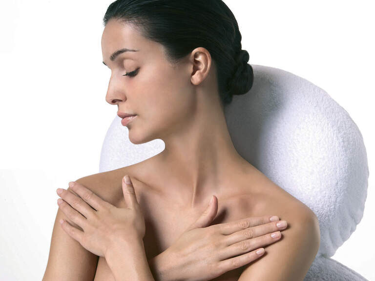 Ein Foto zeigt eine Frau vor einer Kosmetikliege mit weißem Handtuch, die sanft ihre Brust mit den Händen bedeckt.