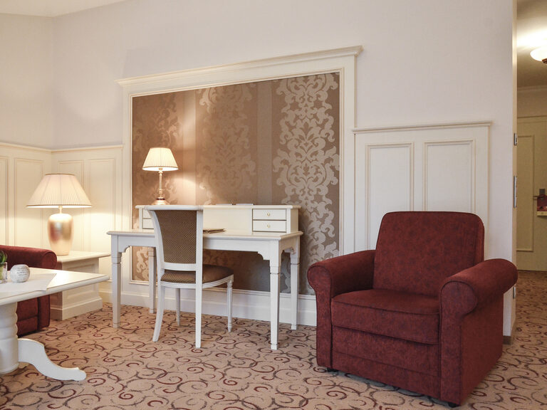 Rot gepolsterte Sessel und ein weißer Scheibtisch im komfortablen Wohnzimmer der Berkhain Suite Deluxe des Wellnesshotels Mooshof im Bayerischen Wald.