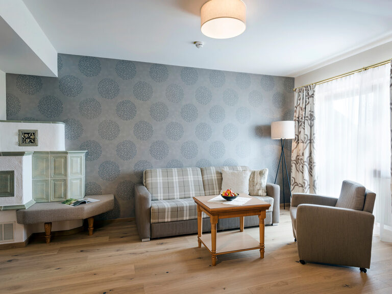 Gemütliches Sofa mit Couchtisch neben einem warmen Kachelofen in der Harlachbergsuite des Wellnesshotels Mooshof in Bodenmais.