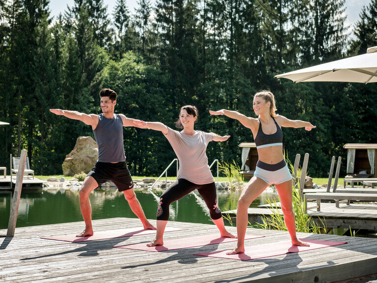 Drei Frauen entspannen beim Yoga am Steg des Naturbadesees