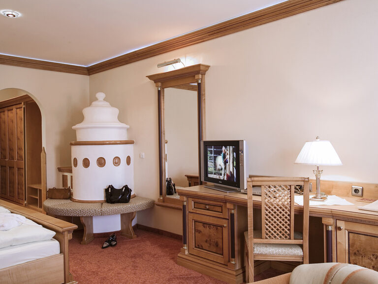 Das bequeme Doppelbett mit Fernseher und Kachelofen gegenüber im Zimmer Typ 10 des Wellnesshotels Mooshof im bayerischen Wald.