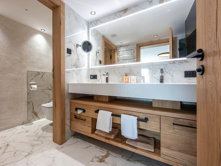 Badezimmer im Zimmer Typ 3A des Wellnesshotels Mooshof im Bayerischen Wald mit einem eleganten Waschbecken und großem Spiegel.