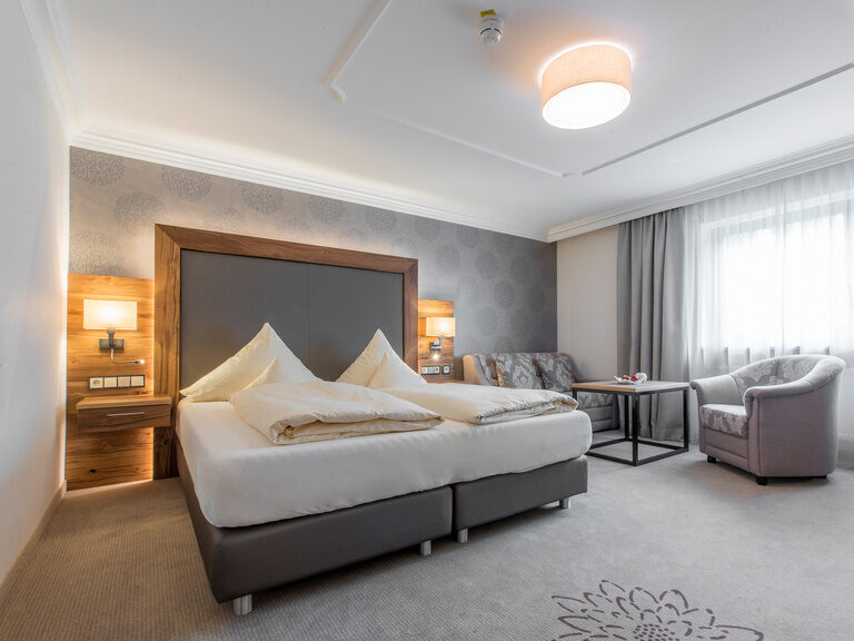 Das gemütliche Hotelzimmer Typ 5 im Wellnesshotel Mooshof im Bayerischen Wald mit einem bequemen Bett und einer Sitzecke direkt am Fenster.