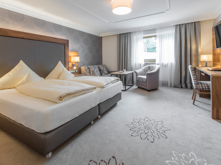 Das stilvoll eingerichtete Zimmer Typ 5 des Wellnesshotels Mooshof im Bayerischen Wald mit einem komfortablen Doppelbett und einem Fernseher neben dem praktischen Arbeitsbereich.