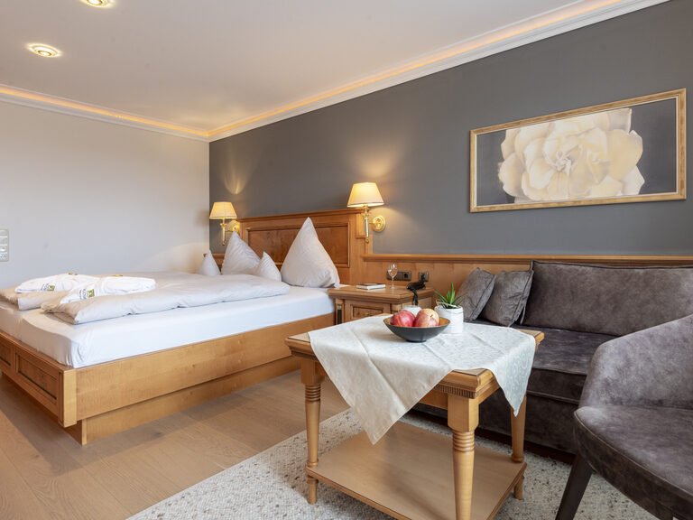 Stilvolles Schlafzimmer im Zimmer Typ 9 des Wellnesshotels Mooshof im Bayerischen Wald mit einem bequemen Bett und einem kuscheligen Sofa.