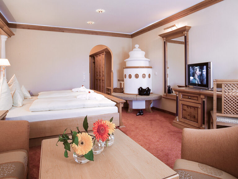 Das geschmackvoll gestaltete Zimmer Typ 10 im Wellnesshotel Mooshof im Bayerischen Wald mit warmen Kachelofen und Wohnecke neben dem Bett.