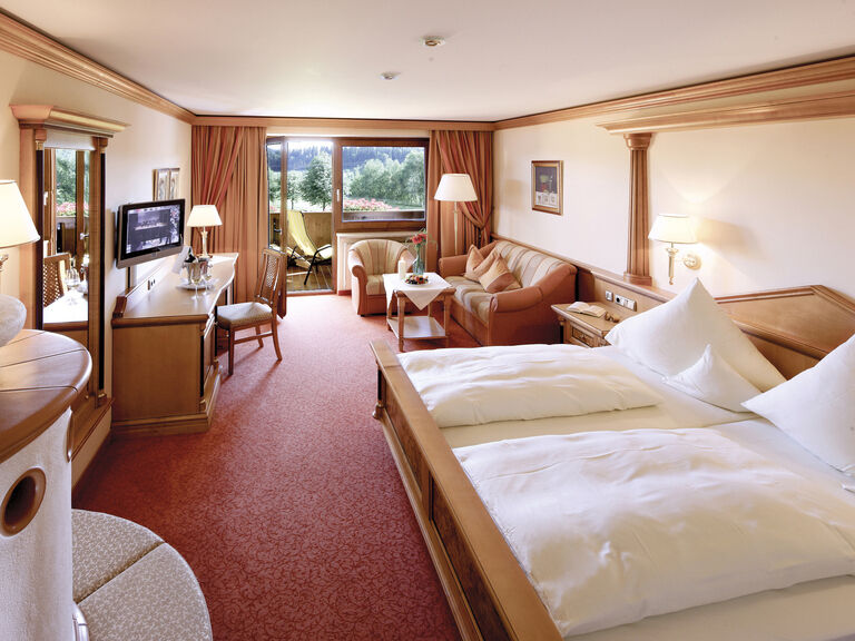 Das Zimmer Typ 10 im Wellnesshotel Mooshof im Bayerischen Wald mit gemütlichen Kachelofen, Wohnecke und Flat-TV vor dem Südbalkon mit Panoramaausblick.