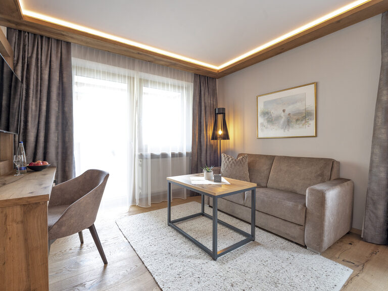 Gemütlicher Wohnbereich im Zimmer Typ 4 des Wellnesshotels Mooshof im Bayerischen Wald, ausgestattet mit modernen Fernseher und bequemer Couch.