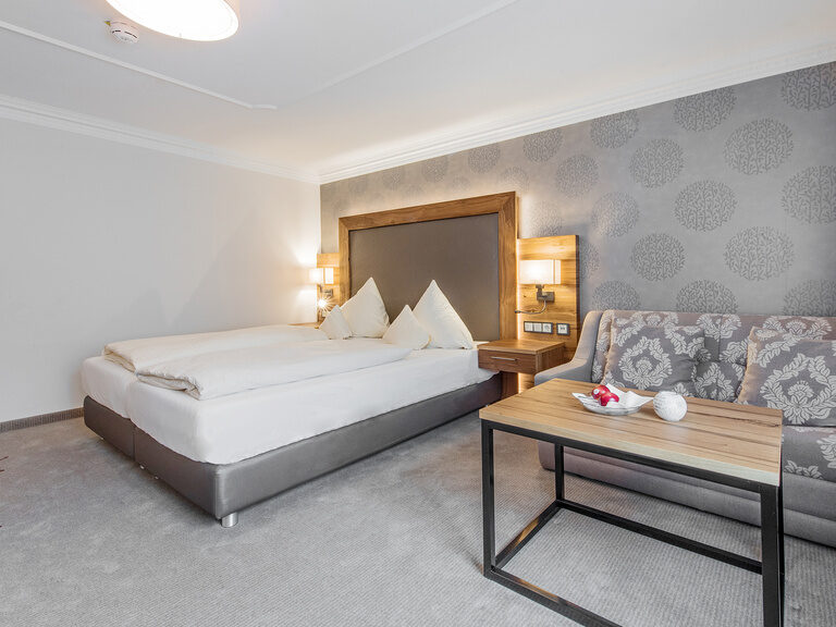 Das einladende moderne Zimmer Typ5 im Wellnesshotel Mooshof in Bodenmais mit gemütlichem Doppelbett und Couch.