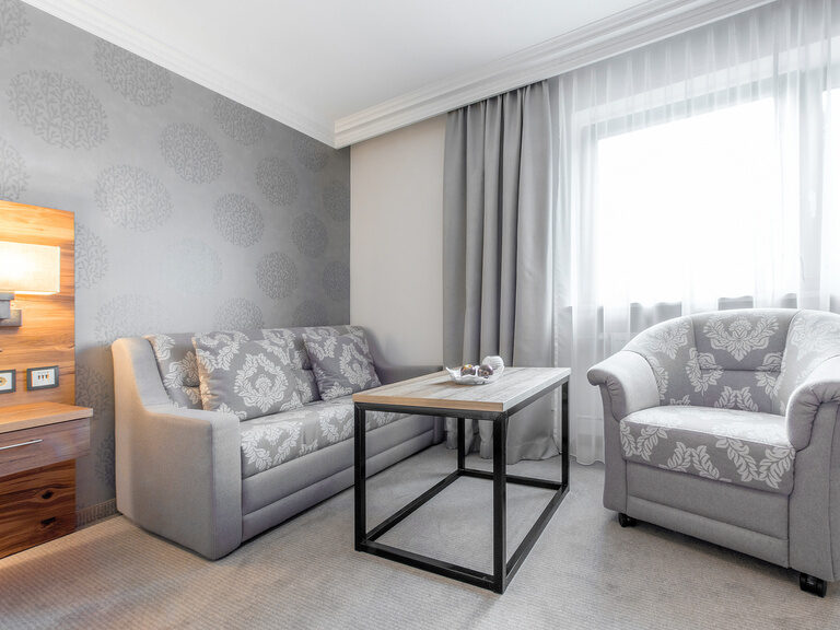 Der Wohnzimmerbereich im Zimmer Typ 5 des Wellnesshotels Mooshof im Bayerischen Wald bietet Komfort mit einem Sessel und einer Couch bei einem funktionalen Couchtisch.